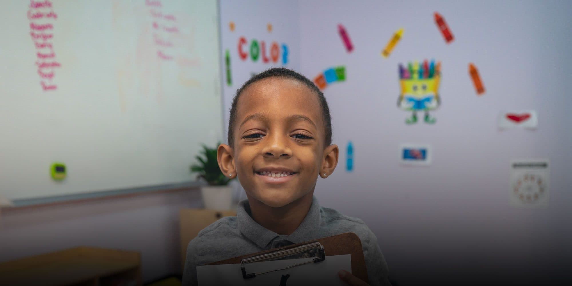 Smiling student holds a clipboard in a classroom.